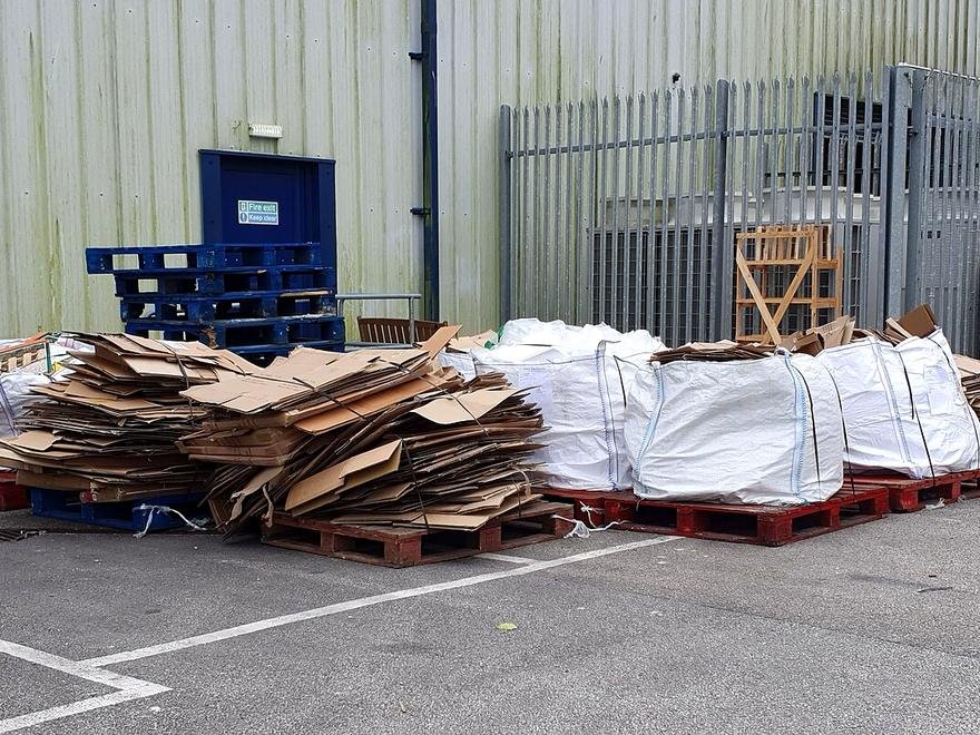 Cartons aplatis et sacs d'emballages posés sur des palettes devant une entreprise, en attente d'enlèvement.